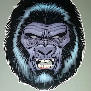 May include: A close-up of a black and blue gorilla mask with a snarling expression. The mask has a detailed design with a textured fur and sharp teeth.