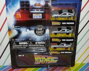 May include: A packaged set of Jada Nano Hollywood Rides die-cast model cars from the Back to the Future movie series. The package includes three miniature silver DeLorean time machines, with the license plate reading "OUTATIME".