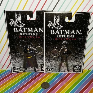 May include: Two Batman Returns keychains featuring Batman and Catwoman figures. The keychains are attached to black cardboard packaging with the Batman logo and the text "Batman Returns Keychain". The figures are approximately 2 inches tall.