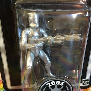 May include: A silver Star Wars Clone Trooper action figure in a plastic blister pack. The figure is holding a blaster rifle and has a 2003 Star Wars logo on the packaging. The packaging also says "Clone Trooper".