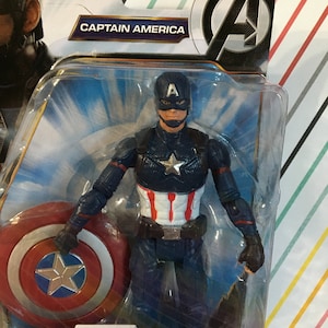 May include: Captain America action figure with a red, white, and blue costume, holding a red, white, and blue shield. The figure is packaged in a plastic blister pack with a blue and white background. The packaging includes the text "CAPTAIN AMERICA".