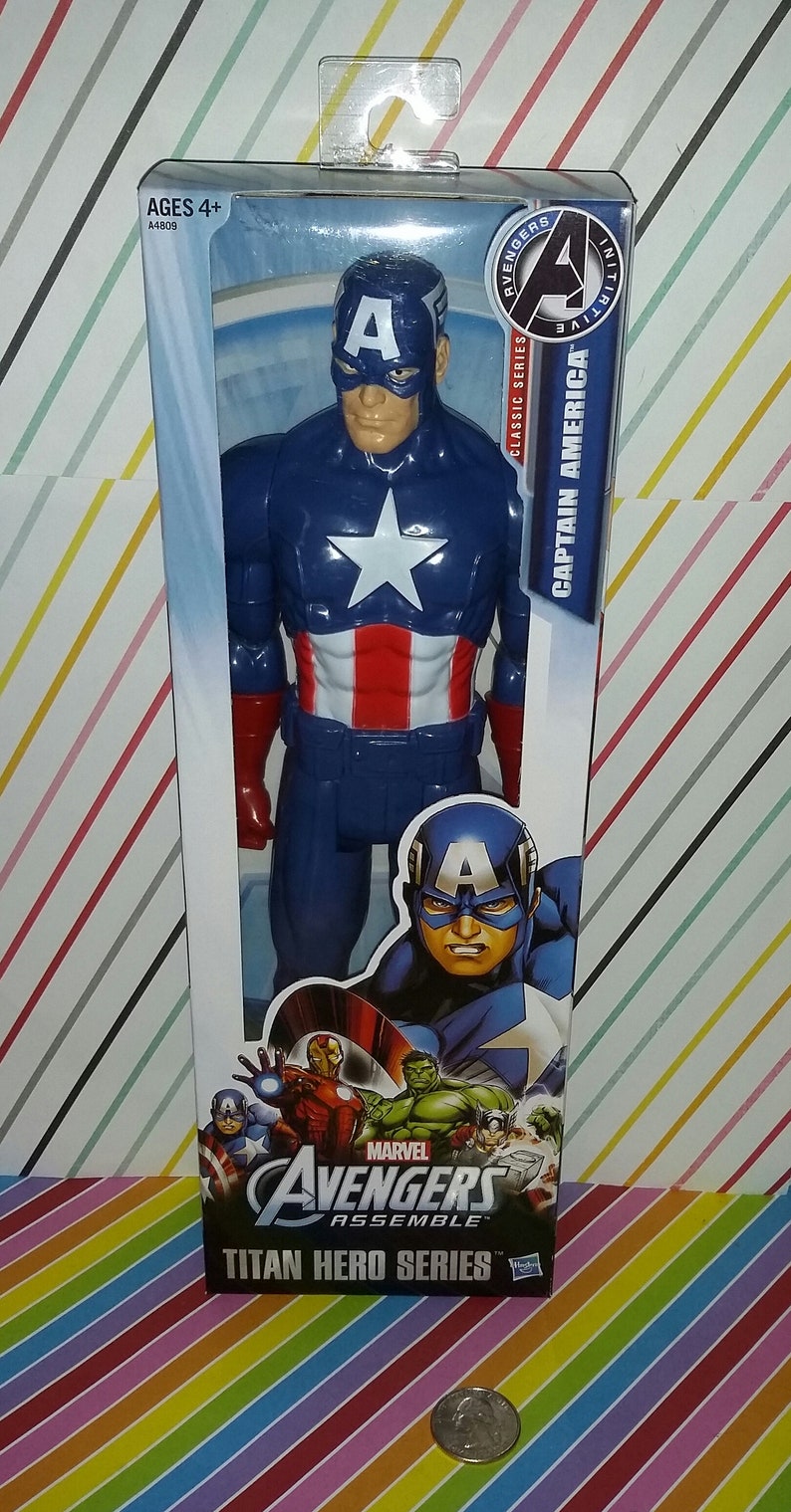 May include: Captain America action figure in a clear plastic package. The figure is blue with a white star on the chest and red and white stripes on the torso. The packaging reads "Avengers Assemble Titan Hero Series."