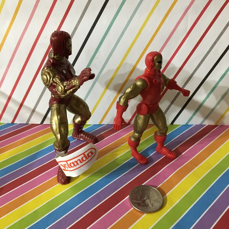May include: Two red and gold Iron Man action figures. The figure on the left has a sticker on its foot that says "Yolanda".