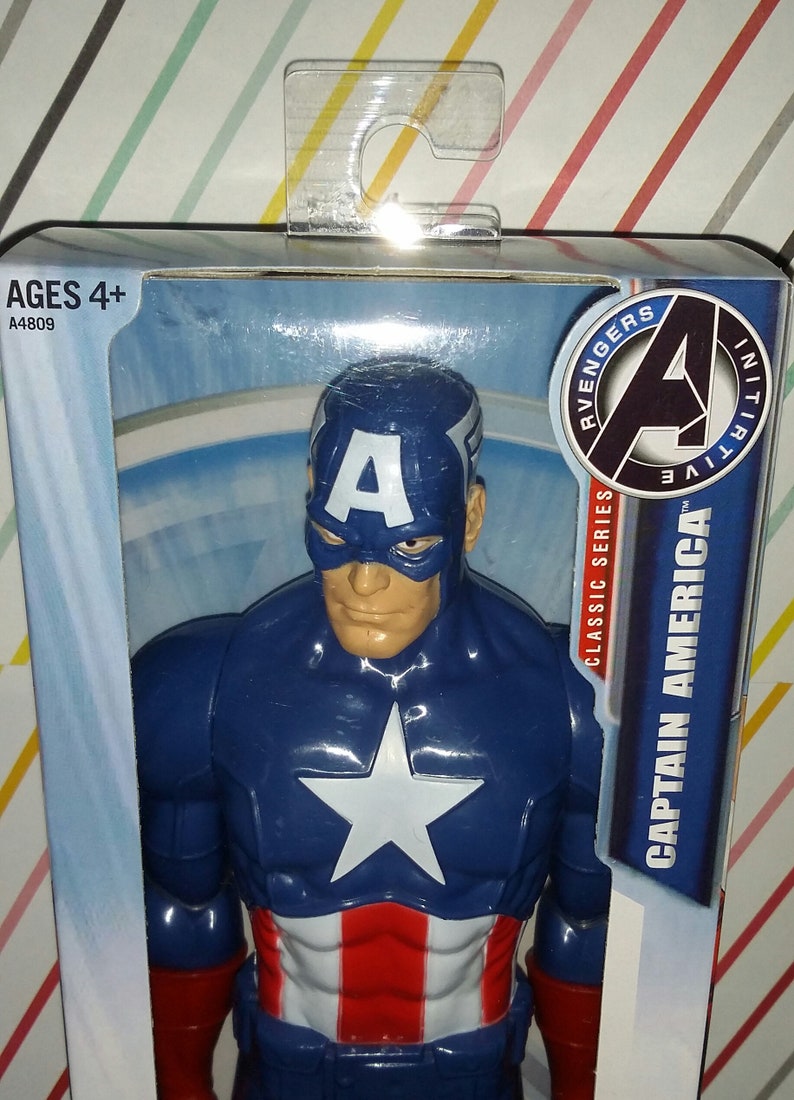 May include: Captain America action figure in a box. The figure is primarily blue with a white star on the chest and red and white stripes on the lower torso. The packaging includes the text "Captain America" and "Avengers Initiative".