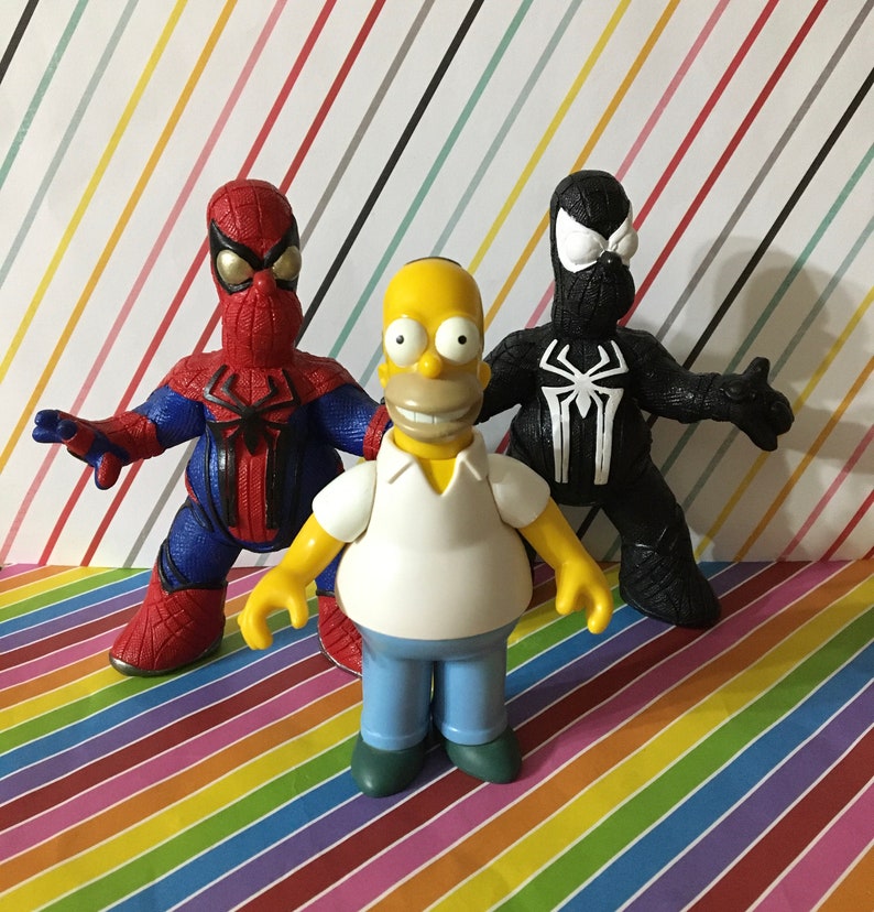 Peut inclure: Une figurine de dessin anim&eacute; jaune avec une chemise blanche et un jean bleu se tient entre une figurine de Spiderman rouge et bleue et une figurine de Spiderman noire. Les figurines sont toutes des jouets en plastique.