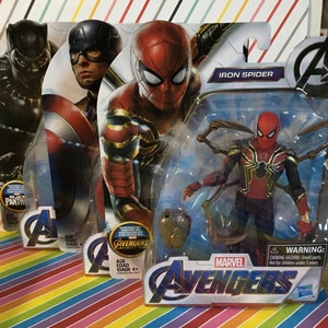 May include: Three action figure packaging boxes featuring Marvel Avengers characters. The boxes are red, blue, and black with images of Iron Spider, Captain America, and Black Panther. The Iron Spider box has the text "Iron Spider" and "Avengers" printed on it. The Captain America box has the text "Avengers" printed on it. The Black Panther box has the text "Black Panther" printed on it.