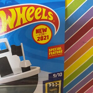 Puede incluir: Un barco de juguete blanco y negro con una bandera negra. El juguete est&aacute; empaquetado en una caja azul y blanca con las palabras "Hot Wheels" y "Nuevo para 2021". La caja tambi&eacute;n tiene el n&uacute;mero "193/250" impreso en ella.