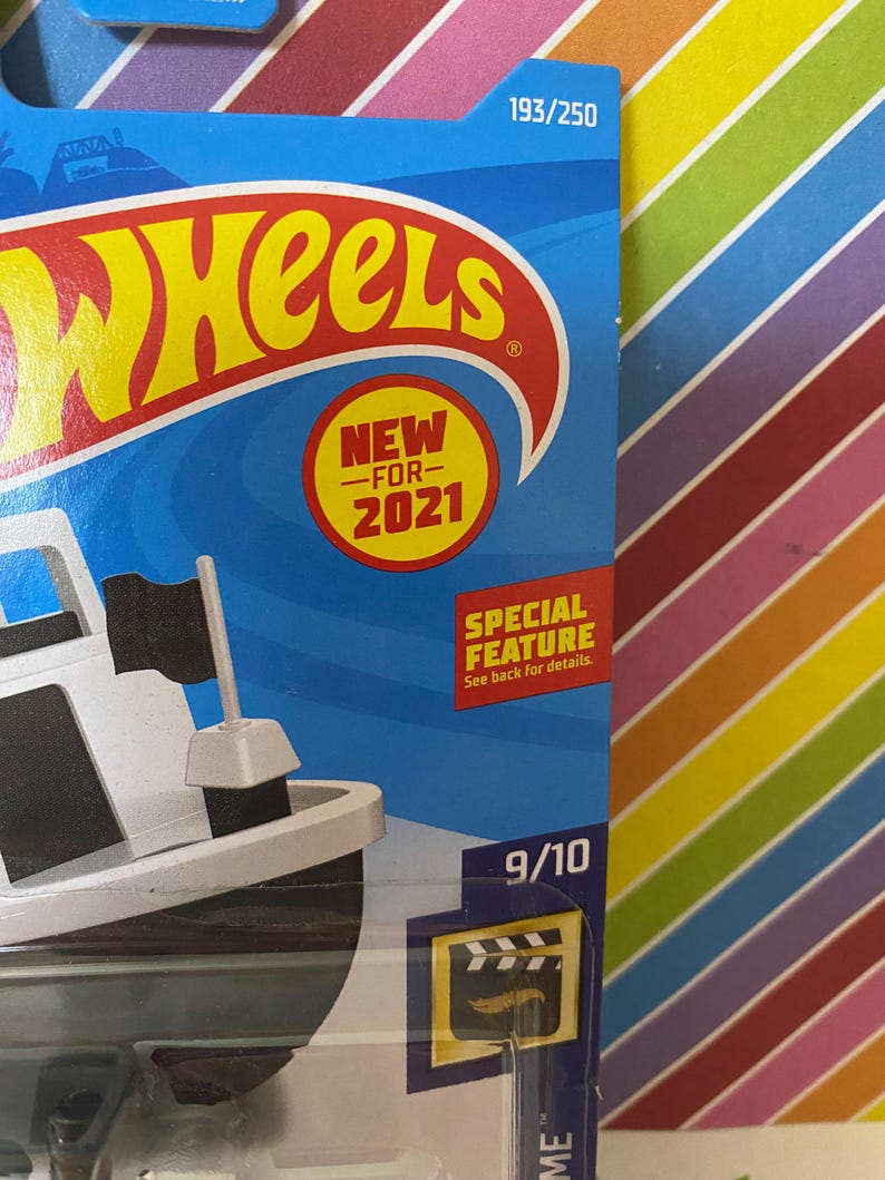 Puede incluir: Un barco de juguete blanco y negro con una bandera negra. El juguete est&aacute; empaquetado en una caja azul y blanca con las palabras "Hot Wheels" y "Nuevo para 2021". La caja tambi&eacute;n tiene el n&uacute;mero "193/250" impreso en ella.