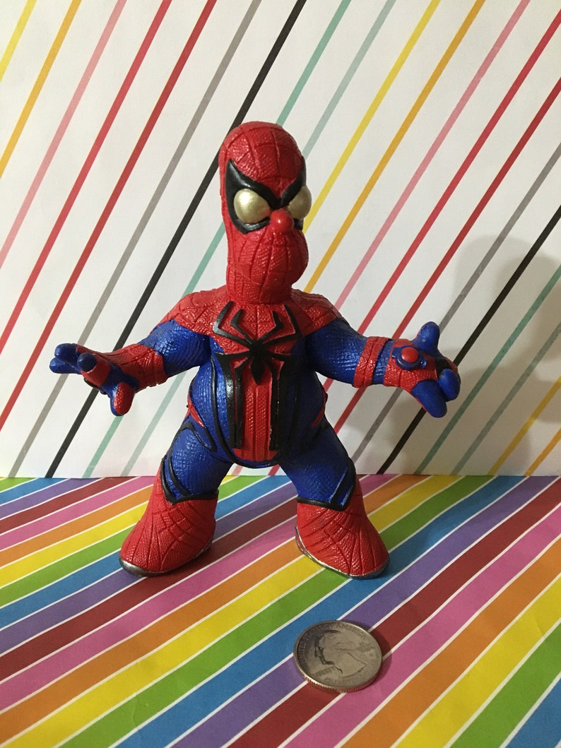 Peut inclure: Une figurine d'action Spider-Man rouge et bleue avec un visage jaune et un motif d'araign&eacute;e noir sur la poitrine. La figurine est debout sur un fond ray&eacute; color&eacute;.