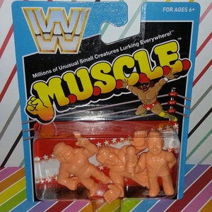 May include: A package of three small plastic figures of wrestlers. The figures are in a clear plastic blister pack on a red and white background. The package is labeled "WWF Muscle" and "Millions of Unusual Small Creatures Lurking Everywhere!" The package is for ages 6 and up.