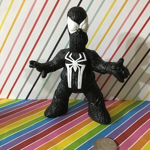 Peut inclure: Figurine d'action en plastique noir et blanc d'un super-h&eacute;ros portant un costume noir avec un motif d'araign&eacute;e blanc. La figurine est debout, les bras tendus.