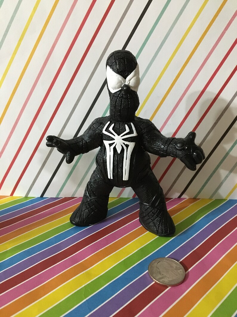 Peut inclure: Figurine d'action en plastique noir et blanc d'un super-h&eacute;ros portant un costume noir avec un motif d'araign&eacute;e blanc. La figurine est debout, les bras tendus.