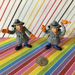 May include: Two gray plastic Inspector Gadget figures with orange gloves and hats. One figure has a gray metal arm with an orange hand.