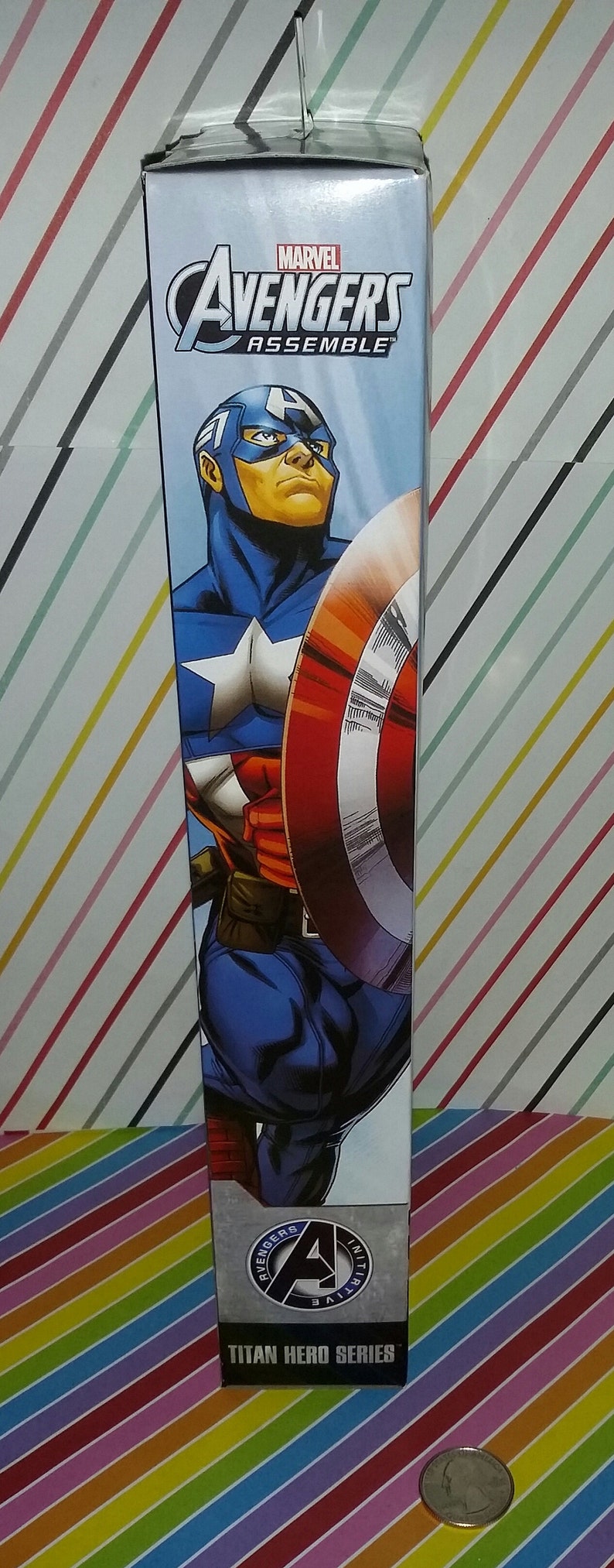 May include: A Marvel Avengers Assemble Titan Hero Series action figure box featuring Captain America. The box is blue with a comic book style illustration of Captain America holding his shield. The box also has the Marvel and Avengers logos.