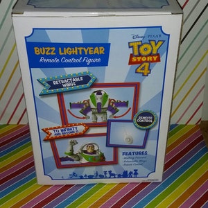 K&ouml;nnte beinhalten: Eine wei&szlig;e Box mit einem farbenfrohen Toy Story 4 Design. Die Box zeigt Buzz Lightyear, einen Weltraum-Ranger, mit einziehbaren Fl&uuml;geln. Auf der Box steht "Buzz Lightyear Fernbedienungsfigur" und "Bis ins Unendliche und dar&uuml;ber hinaus!" Die Box zeigt auch "Eigenschaften: Vorw&auml;rts gehen, Einziehbare Fl&uuml;gel, Fernbedienung".