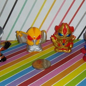 May include: Four small plastic action figures of characters from the Ultraman series. The figures are silver, yellow, red, and blue. The figures are posed in action stances.