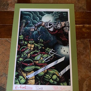 May include: A framed print featuring the Teenage Mutant Ninja Turtles battling Shredder. The artwork showcases the turtles with red bandanas, wielding weapons against Shredder in a dark, urban setting. Signed by the artists.