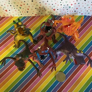 May include: Six colorful rubber monster toys with large eyes and open mouths. The toys are made of a soft, flexible material and are in various colors, including orange, yellow, green, purple, and brown.