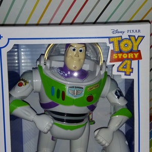 K&ouml;nnte beinhalten: Eine wei&szlig;e, gr&uuml;ne und violette Buzz Lightyear Actionfigur aus dem Film Toy Story 4. Die Figur befindet sich in einer Box mit dem Toy Story 4 Logo und den Worten "Disney Pixar" darauf. Die Box tr&auml;gt au&szlig;erdem die Aufschrift "8+."