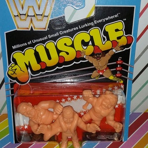 May include: A plastic package with three small, orange, wrestler figures. The package has a red background with white stars and the words "MUSCLE" in yellow letters. The package also has a blue header with the words "FOR AGES 6+" and "Millions of Unusual Small Creatures Lurking Everywhere!&trade;".