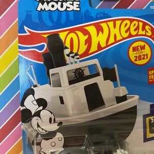 Puede incluir: Un coche de juguete Hot Wheels blanco con Mickey Mouse como capit&aacute;n de un barco de vapor. El coche est&aacute; en una tarjeta azul y amarilla con las palabras "Disney Mickey Mouse Hot Wheels" y "Nuevo para 2021".