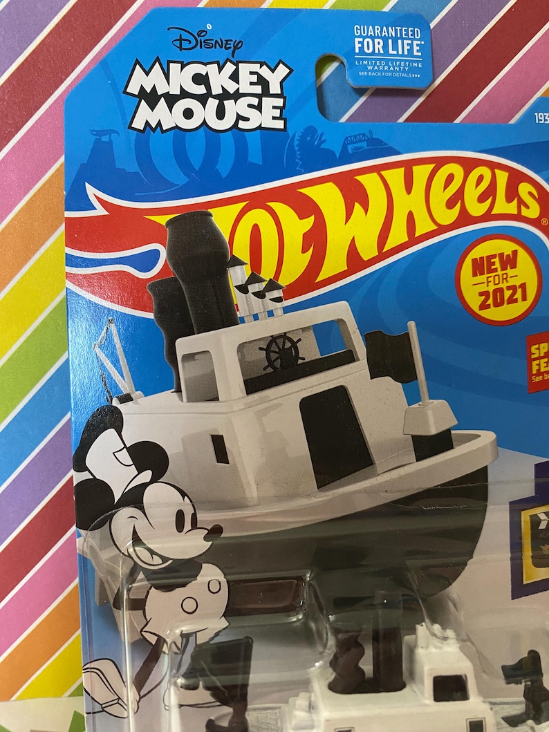 Puede incluir: Un coche de juguete Hot Wheels blanco con Mickey Mouse como capit&aacute;n de un barco de vapor. El coche est&aacute; en una tarjeta azul y amarilla con las palabras "Disney Mickey Mouse Hot Wheels" y "Nuevo para 2021".