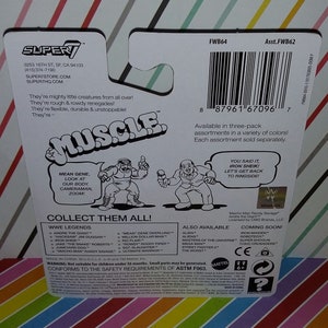 May include: A colorful cardboard box featuring a wrestling figure toy. The box has a white background with red and black stripes. The front of the box features a cartoon image of a wrestler with the words "MUSCLE" in large, bold letters. The back of the box lists various wrestling figures available in the collection. The box also includes a warning that the toy is not suitable for children under 36 months.