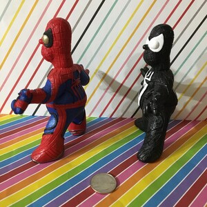 Peut inclure: Deux petites figurines peintes &agrave; la main de Spider-Man et Venom. Spider-Man est rouge et bleu avec des d&eacute;tails noirs. Venom est noir avec des yeux blancs. Les figurines sont debout sur un fond ray&eacute; color&eacute;.