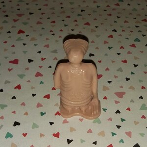 May include: A small, beige plastic figurine of an alien with a large head and a thin body. The figurine is in a kneeling position with its hands clasped together. The figurine is made by Universal City Studios.