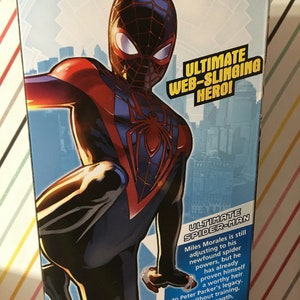 May include: A comic book cover featuring a red and black superhero with a spider symbol on their chest. The text on the cover reads "Ultimate Web-Slinging Hero!" and "Ultimate Spider-Man".