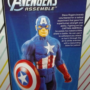 May include: A Captain America action figure in a blue and red costume, holding a shield. The figure has a white star on the chest and a mask. The text on the packaging reads "Avengers Assemble".