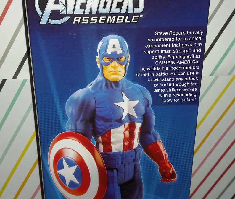 May include: A Captain America action figure in a blue and red costume, holding a shield. The figure has a white star on the chest and a mask. The text on the packaging reads "Avengers Assemble".