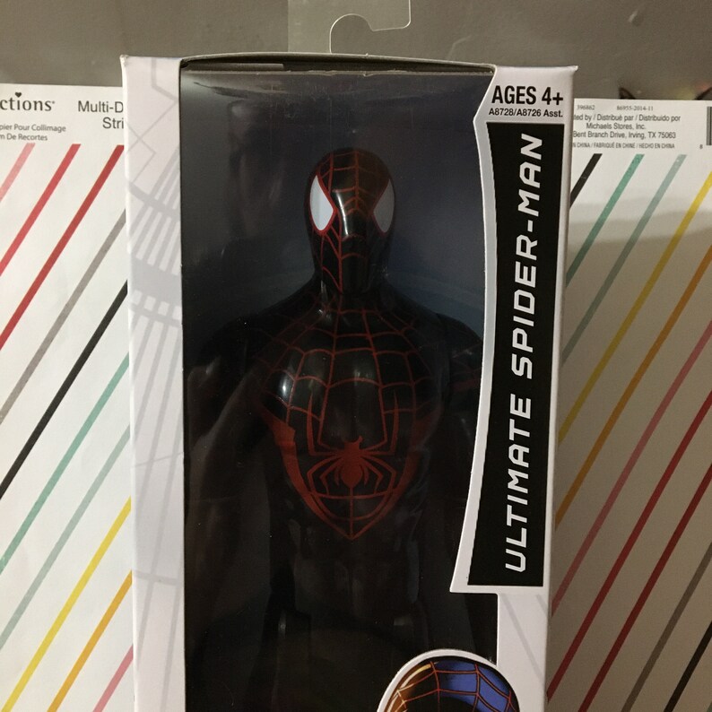 May include: A black and red action figure of Ultimate Spider-Man. The figure has a red spider symbol on its chest and is posed with its arms outstretched. The packaging says "Ages 4+" and "Ultimate Spider-Man".