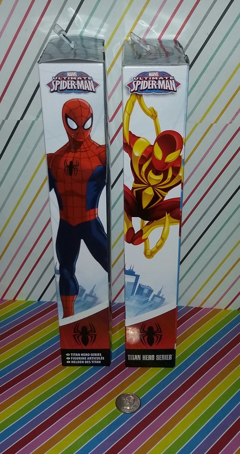 May include: Two cardboard boxes with images of Spider-Man on them. The boxes are red, blue, and yellow. The text on the boxes reads "MARVEL ULTIMATE SPIDER-MAN" and "TITAN HERO SERIES".