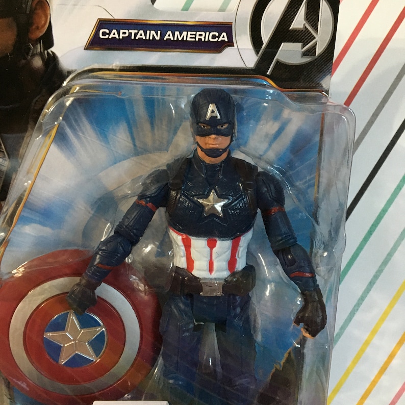May include: Captain America action figure with a red, white, and blue costume, holding a red, white, and blue shield. The figure is packaged in a plastic blister pack with a blue and white background. The packaging includes the text "CAPTAIN AMERICA".
