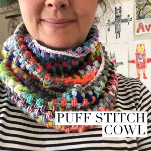 May include: A colorful crocheted cowl with a puff stitch pattern. The cowl is made with a variety of colors, including pink, blue, green, yellow, and orange. The text "PUFF STITCH COWL" is printed on the bottom of the image.