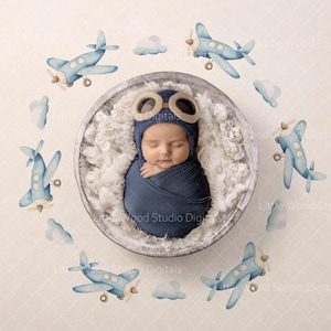 May include: A newborn baby wrapped in a navy blue blanket and wearing a pilot hat with goggles, nestled in a wooden bowl filled with white fluff. Watercolor airplanes and clouds surround the bowl, creating an aviation theme.
