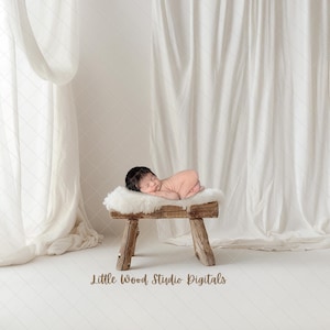 Puede incluir: Un bebé recién nacido durmiendo sobre una alfombra de piel sintética blanca en un taburete de madera. El taburete tiene un acabado de madera natural y está colocado sobre un fondo blanco con cortinas blancas transparentes.
