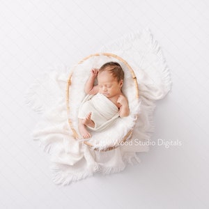 Puede incluir: Un bebé recién nacido duerme plácidamente en una cesta tejida, envuelto en una manta blanca. La cesta está sobre una manta blanca y esponjosa con flecos.