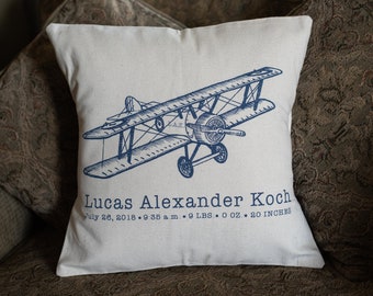 May include: A white pillow with a blue airplane design and the text "Lucas Alexander Koch July 26, 2018 9:35 am 9 LBS. O OZ.. 20 INCHES".