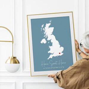 May include: A framed print of a map of the United Kingdom with a red heart marking a location. The text below the map reads "Home Sweet Home 51°25'45.6"N 0°09'12.9"W".