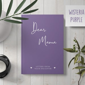 Pu&ograve; includere: Diario viola con il testo "Dear Mama" e "Letters from your daughter" in bianco. Il diario &egrave; su una superficie di legno bianco con un vaso di foglie verdi e un portacandele.