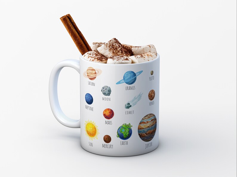 Pu&ograve; includere: Una tazza in ceramica bianca con un'illustrazione colorata dei pianeti del nostro sistema solare, inclusi il sole, la luna e una cometa. La tazza &egrave; piena di cioccolata calda e marshmallow e ha un bastoncino di cannella che sporge dalla parte superiore.
