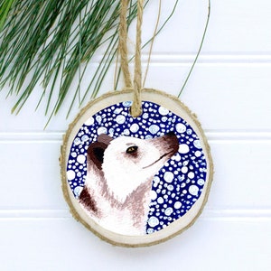 May include: A round wooden ornament with a blue background and white polka dots. A painted white and brown animal with black eyes and a pink nose is in the center of the ornament.