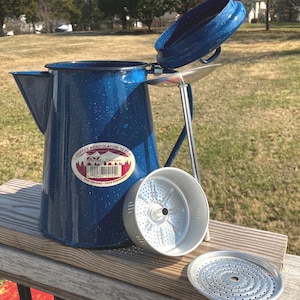 May include: Blue speckled enamel coffee percolator with a 12-cup capacity. The lid is open, revealing the interior. The percolator includes a filter basket and a perforated plate. The label reads "Coffee Percolator - 12 Cup".