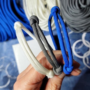 May include: Three paracord bracelets in white, gray, and blue. The bracelets are tied together in a knot.