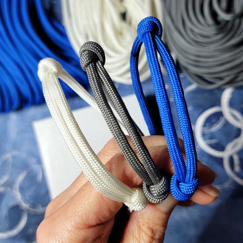 May include: Three paracord bracelets in white, gray, and blue. The bracelets are tied together in a knot.
