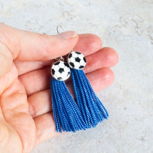 hand holding royal blue tassel earrings with black and white soccer ball charms