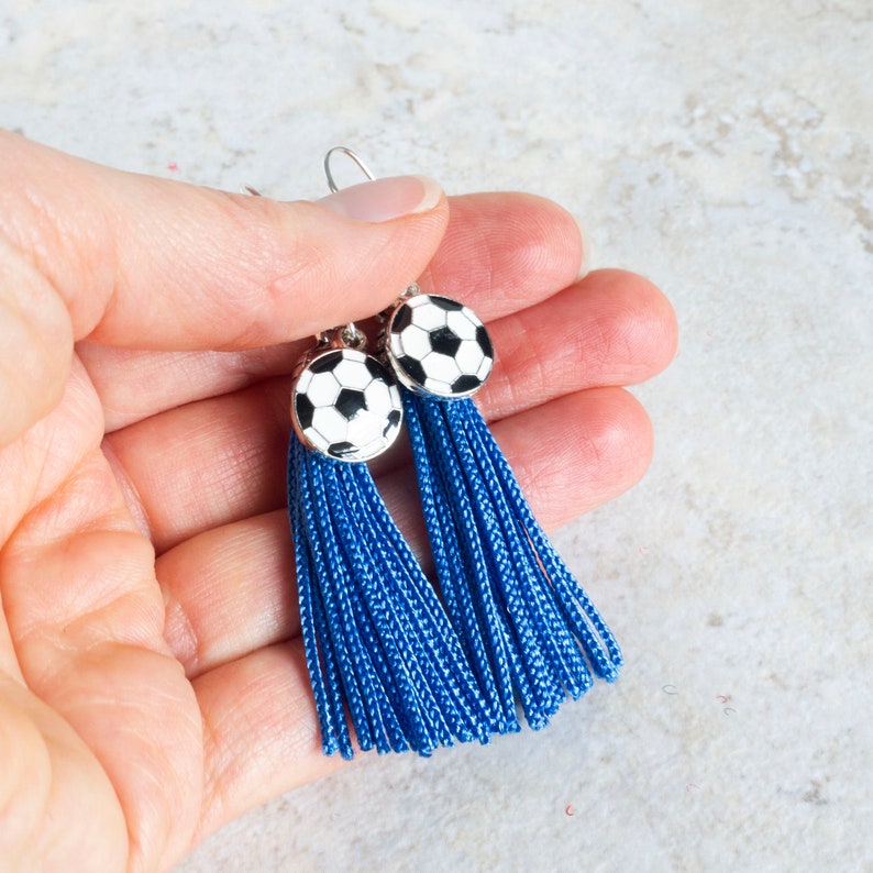 hand holding royal blue tassel earrings with black and white soccer ball charms