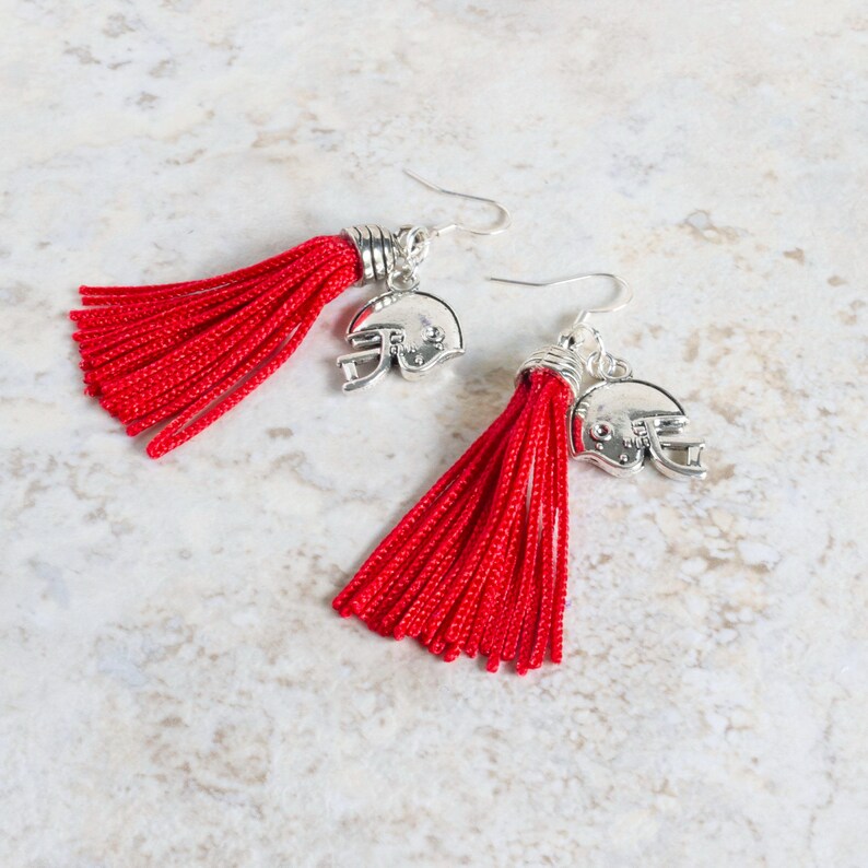 May include: A pair of red tassel earrings with silver football helmet charms.